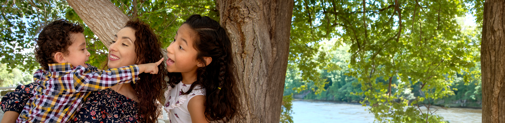 mother and two children laughing under a tree and by a river