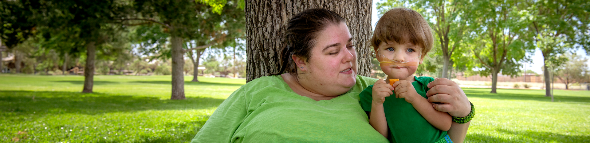 Mom and her child at a park, and the child is wearing an oxygen tube.