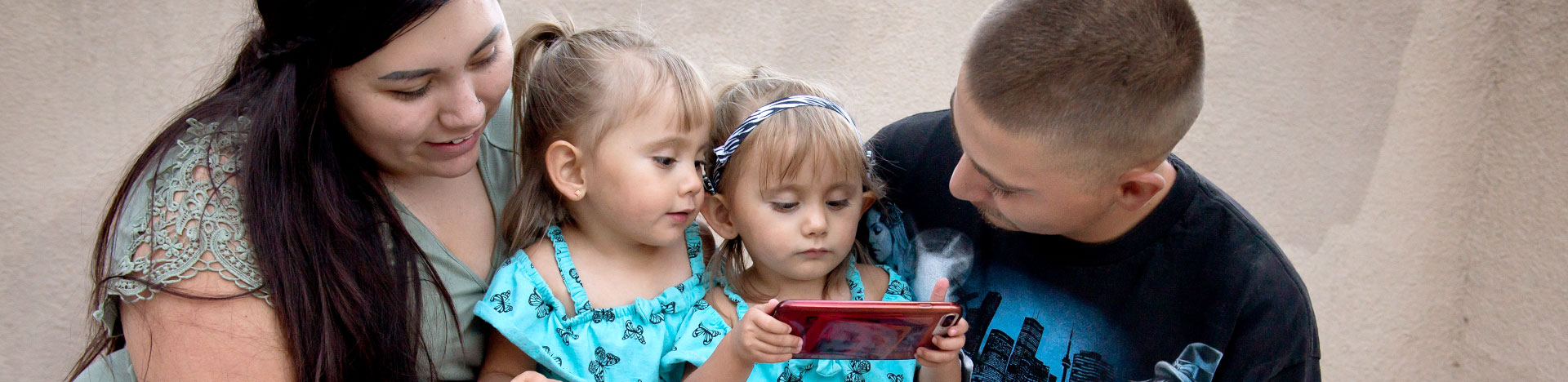 parents and their twin daughters using a cell phone, an example of assistive technology