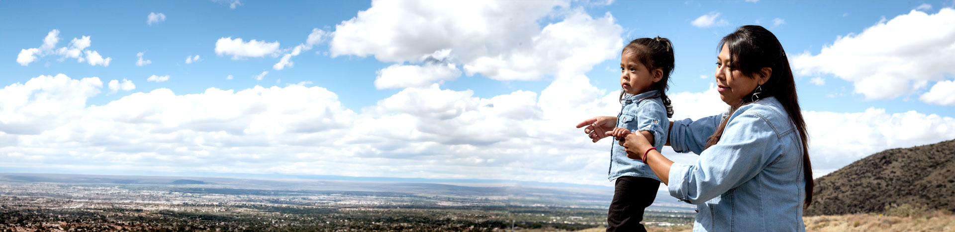 A native american woman with her toddler in front of a wide city-scape