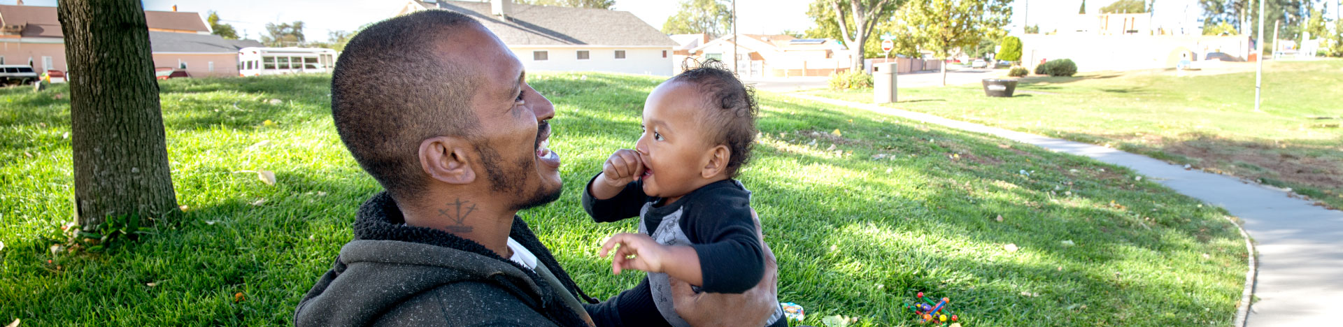 A father holding his toddler and laughing in a park